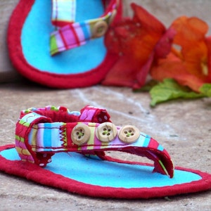 May include: A pair of blue and red fabric sandals with colorful striped straps and wooden button accents.