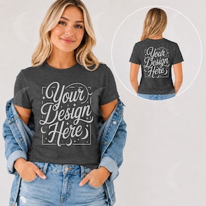 May include: A dark gray short-sleeve t-shirt featuring the white text Your Design Here in a decorative script font inside a rectangular frame with small star and moon accents. The shirt is layered under a blue denim jacket with metal buttons.