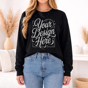 May include: A black long-sleeve shirt with the text "Your Design Here" in a white, decorative font. The shirt is paired with blue jeans. The design is centered on the front of the shirt.