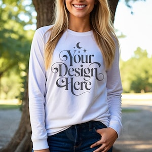 May include: A white long-sleeve shirt with the text "Your Design Here" in a decorative script. The shirt is paired with blue jeans. The design includes a crescent moon and stars.