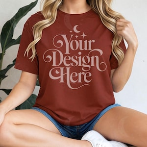 May include: A maroon t-shirt with the text "Your Design Here" in a decorative font. The shirt is short-sleeved and appears to be made of a soft material. The model is wearing blue denim shorts.