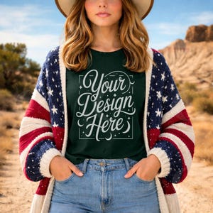 May include: A person wearing a dark green t-shirt with the text "Your Design Here" in white script. The person is also wearing a red, white, and blue cardigan and blue jeans. A brown hat is on the person's head.