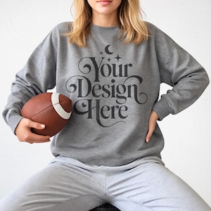 May include: A gray sweatshirt with the text "Your Design Here" in a decorative font. The person is holding a brown and white football. The sweatshirt and sweatpants are a matching set.