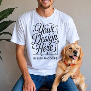 Può includere: Maglietta bianca con la scritta "Your Design Here" in corsivo decorativo, con la scritta "BY LUNARMOCKUPS" sotto. Un cane golden retriever con collare arancione è seduto in grembo. La persona indossa jeans blu.