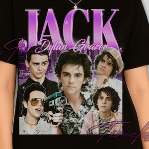 May include: Black t-shirt featuring a graphic of Jack Dylan Grazer with the name "JACK" in a purple gradient font. The shirt showcases multiple images of the actor. The shirt is a classic crew neck style.