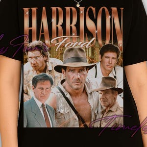 May include: Black t-shirt featuring a collage of Harrison Ford images with the text "HARRISON FORD" in a gold metallic font. The shirt has a crew neck and short sleeves. The overall theme is vintage movie memorabilia.