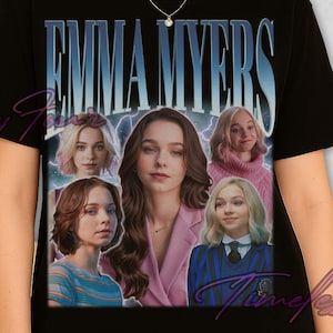 May include: Black t-shirt with the name "EMMA MYERS" in a blue gradient font. The shirt features a collage of images of a woman. The t-shirt is worn by a person wearing black sunglasses.