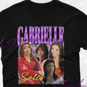 Puede incluir: Camiseta negra con un gráfico de estilo vintage que presenta a un grupo de mujeres con el texto "Gabrielle Solis" en morado y amarillo.