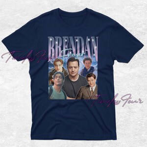 May include: Navy blue t-shirt featuring a collage of images of Brendan Fraser, with the name "Brendan Fraser" in a stylized font. The design includes multiple photos of the actor against a blue and purple background.