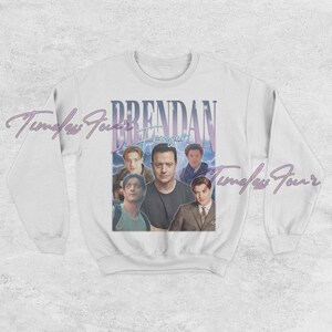 May include: White crewneck sweatshirt featuring a graphic of actor Brendan Fraser with the text "Brendan Fraser" in a vintage style. The design includes multiple images of the actor in various poses, with a blue and purple color scheme.