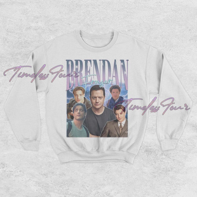 May include: White crewneck sweatshirt featuring a graphic of actor Brendan Fraser with the text "Brendan Fraser" in a vintage style. The design includes multiple images of the actor in various poses, with a blue and purple color scheme.