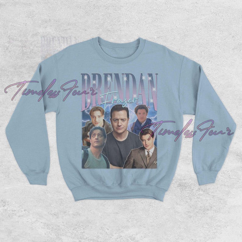 May include: Light blue sweatshirt featuring a collage of images of Brendan Fraser. The name "Brendan Fraser" is printed in a retro font above the images. The sweatshirt has long sleeves and a crew neck.