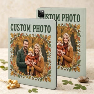May include: Two light green tablet cases featuring the text CUSTOM PHOTO at the top and a central rectangular frame surrounded by an illustration of autumn leaves and acorns. Each case displays a photograph of a family with a baby.