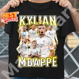 May include: Black t-shirt featuring a graphic of Kylian Mbapp&eacute; in a white soccer jersey. The design includes multiple images of the player, the name "KYLIAN MBAPPE" in yellow, and a "BEST SELLER" sticker.