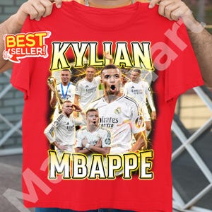 May include: Red t-shirt featuring a collage of images of Kylian Mbapp&eacute; in a white jersey. The text "KYLIAN MBAPPE" is displayed in yellow with a lightning bolt effect. A "BEST SELLER" sticker is in the upper left corner.
