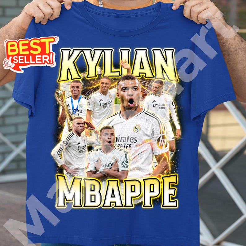 May include: Royal blue t-shirt featuring a graphic of Kylian Mbapp&eacute; with the text "KYLIAN MBAPPE" in yellow. The design includes images of the soccer player in a white jersey. A "BEST SELLER" sticker is in the upper left corner.