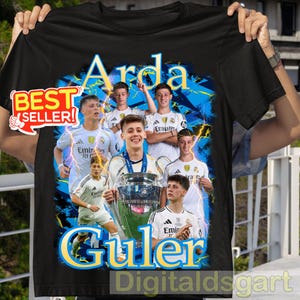 May include: Black t-shirt featuring a collage of images of a soccer player, with the name "Arda Guler" in yellow and blue text. The shirt also has the text "BEST SELLER!" in a red and white sticker.