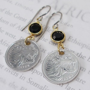 May include: Gold earrings with black gemstone accents and silver coin charms featuring a lion's head. The coins have the text "1 Shilling" and "1962" on them.