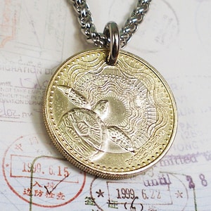 May include: A gold-toned pendant necklace featuring a detailed design of two sea turtles swimming towards a sun. The pendant is attached to a silver chain.