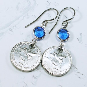 May include: A pair of silver earrings with blue gemstone accents. Each earring features a silver coin with the inscription "Banco de Guatemala" and "5 Centavos de Quetzal" and the year "1994".