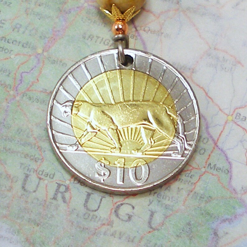 K&ouml;nnte beinhalten: Eine silberne und goldene M&uuml;nze mit einem goldenen Tier und dem Text "$10" darauf. Die M&uuml;nze liegt auf einer Karte von Uruguay.