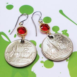 May include: A pair of silver earrings with red glass beads and Thai baht coins featuring a temple. The coins have Thai text that reads "1 Baht".