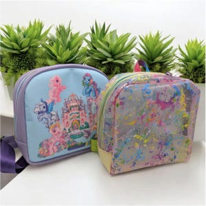 May include: Two My Little Pony backpacks. One is blue with a castle and ponies, the other is clear with colorful paint splatters.