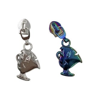 May include: Two metal zipper pulls featuring a character design of a small teacup with a handle and base. One pull is finished in a polished silver tone, while the other features an iridescent, multi-colored metallic finish with blue and purple hues.