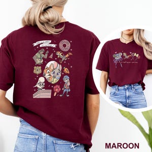 May include: A maroon short-sleeve t-shirt featuring Zootopia character graphics on the back and front. The back design includes various characters, a badge, a donut, and the text "You can be whatever you wish to be." The front features smaller icons.