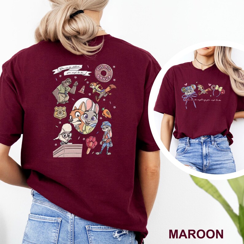 May include: A maroon short-sleeve t-shirt featuring Zootopia character graphics on the back and front. The back design includes various characters, a badge, a donut, and the text "You can be whatever you wish to be." The front features smaller icons.