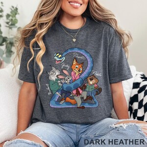 Puede incluir: Una camiseta gris jaspeado oscuro con un estampado gr&aacute;fico de personajes de dibujos animados, incluyendo un zorro, un conejo, una serpiente, un lince y un castor. Los nombres Judy, Nick y Nibbles est&aacute;n escritos en cursiva cerca de ellos.