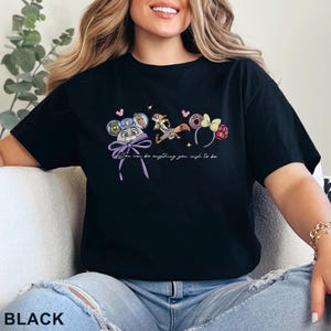 May include: A black short-sleeve t-shirt featuring a graphic print of a rabbit character with a police badge, a fox character, and two sets of mouse-style ears. The text "You can be anything you wish to be" is printed in white below the illustrations.