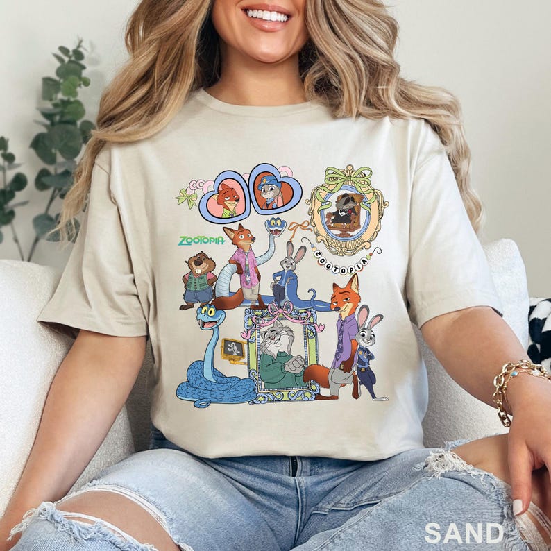 May include: Sand-colored t-shirt featuring a colorful graphic of characters from the animated film "Zootopia." The design includes framed portraits of the characters and the film's title. The shirt is made of a soft material.