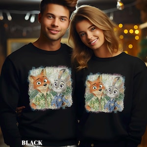 Puede incluir: Sudaderas negras con un gr&aacute;fico colorido de Nick Wilde y Judy Hopps de Zootopia. La imagen muestra a los personajes con sus uniformes. La palabra "BLACK" est&aacute; impresa en la parte inferior de la sudadera.