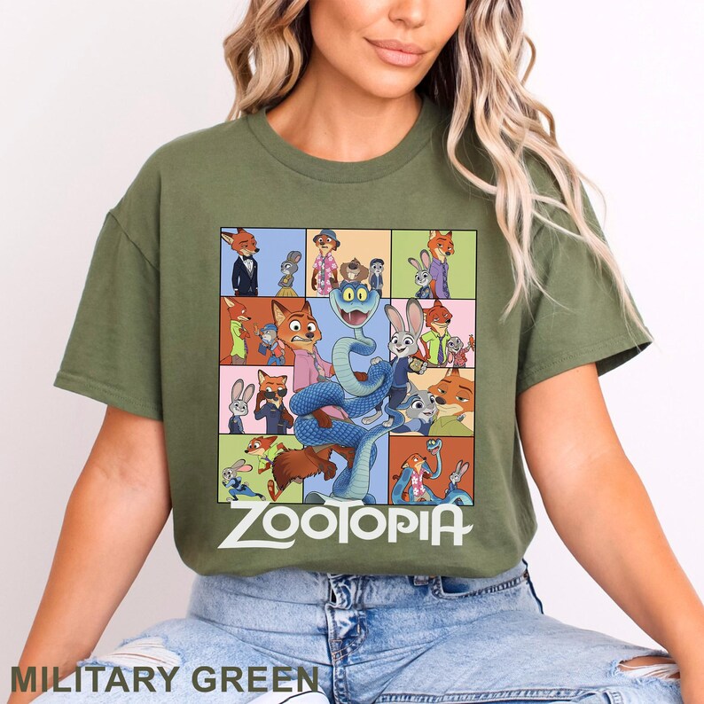 May include: An olive green t-shirt featuring a large rectangular graphic print with multiple scenes of animated characters from Zootopia. The design includes a central blue snake surrounded by various character panels and the white Zootopia logo text.