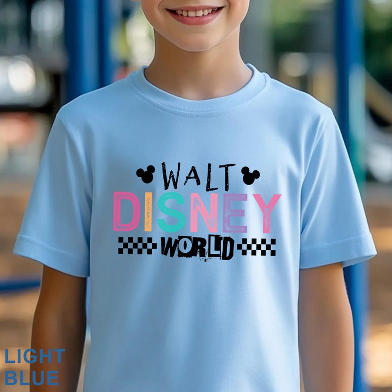 Pu&ograve; includere: Una t-shirt a maniche corte color azzurro con la scritta Walt Disney World in lettere nere, rosa, gialle e turchesi. Il design include due sagome nere di orecchie di Topolino e un bordo a scacchi bianco e nero.