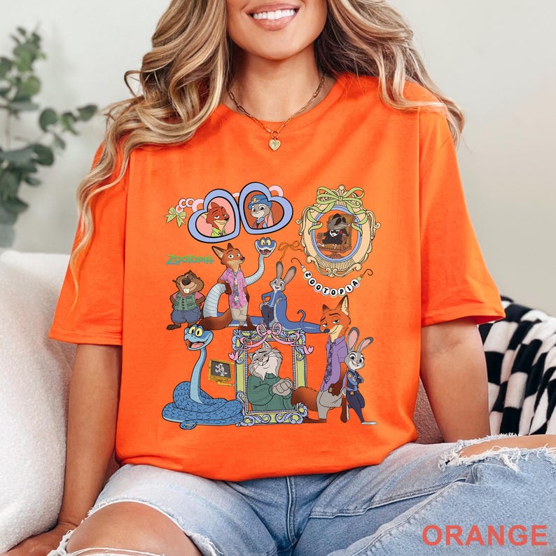 May include: Orange t-shirt featuring a colorful graphic of characters from the animated movie Zootopia. The design includes various characters in ornate frames and the word "Zootopia". The shirt is made of a soft material and has short sleeves.