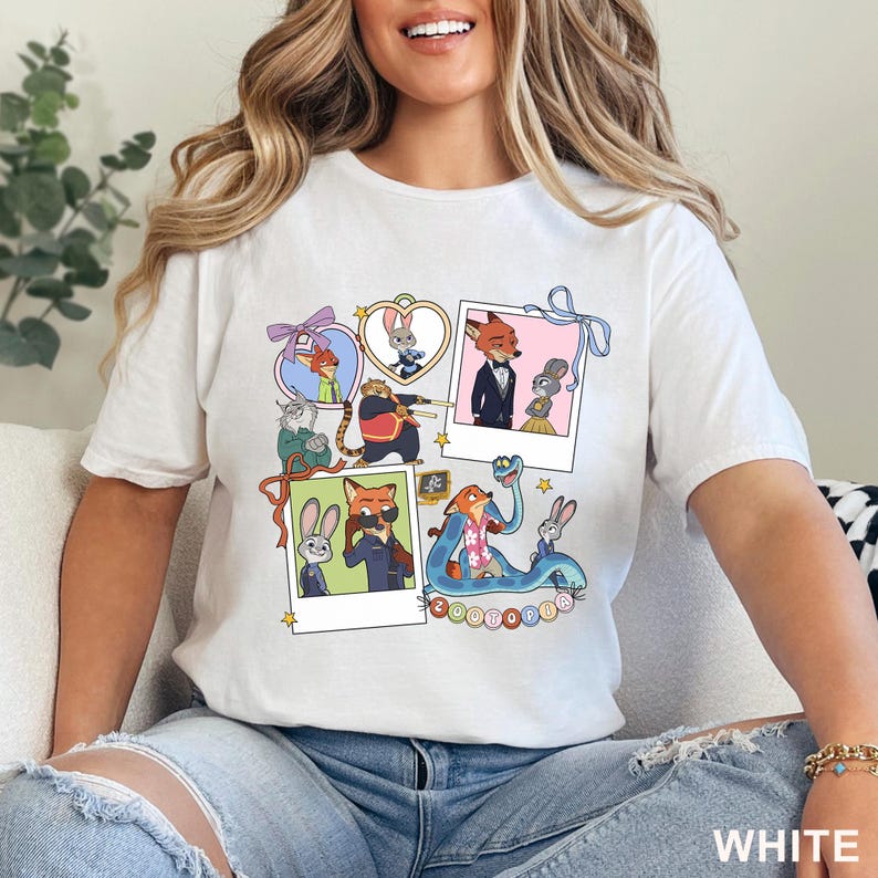 May include: A white t-shirt featuring a graphic print of Zootopia characters in various frames, including polaroids and heart-shaped borders. The design displays Nick Wilde and Judy Hopps in multiple scenes, along with other characters, and the word Zootopia.