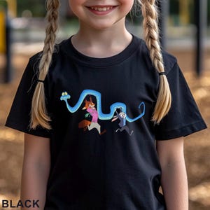 May include: A black short-sleeved t-shirt featuring a graphic print of a long, winding blue snake wrapping around two cartoon characters. The characters include a fox wearing a pink shirt and a rabbit wearing a blue jacket. The word BLACK is printed.