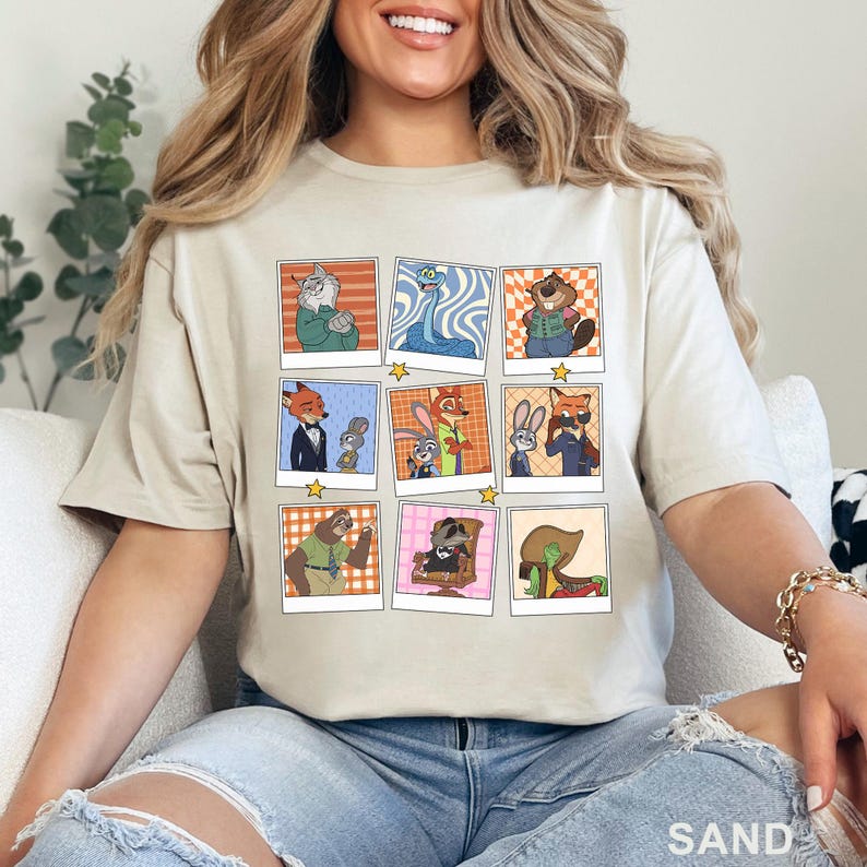 Pode incluir: Camiseta cor de areia com uma grade de retratos de personagens de desenhos animados em molduras estilo polaroid. Os retratos retratam v&aacute;rios personagens de animais em poses diferentes. A palavra "SAND" &eacute; impressa na parte inferior.
