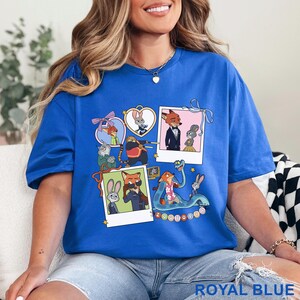 May include: A royal blue t-shirt featuring a graphic print of Zootopia characters including Judy Hopps and Nick Wilde. The design includes multiple polaroid-style frames, heart-shaped borders, and various scenes of the animated animals.