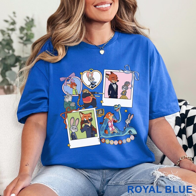 May include: A royal blue t-shirt featuring a graphic print of Zootopia characters including Judy Hopps and Nick Wilde. The design includes multiple polaroid-style frames, heart-shaped borders, and various scenes of the animated animals.