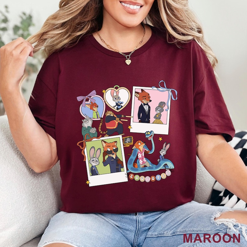 May include: A maroon short-sleeved t-shirt featuring a graphic print of Zootopia characters including Nick Wilde and Judy Hopps. The design includes multiple polaroid-style frames, heart-shaped borders, and a blue snake, with the text Zootopia.