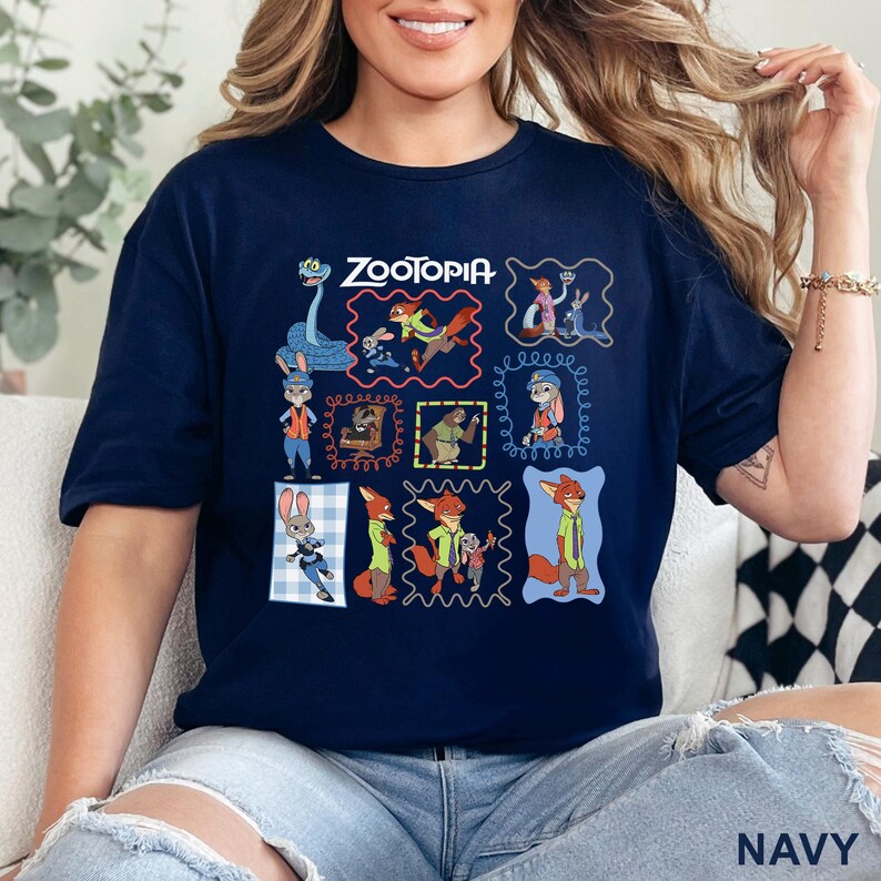 K&ouml;nnte beinhalten: Ein marineblaues Kurzarm-T-Shirt mit einem Grafikdruck verschiedener Charaktere aus dem Film Zoomania. Das Design enth&auml;lt mehrere gerahmte Illustrationen von Judy Hopps und Nick Wilde in verschiedenen Posen, mit dem Zoomania-Logo am oberen Rand.