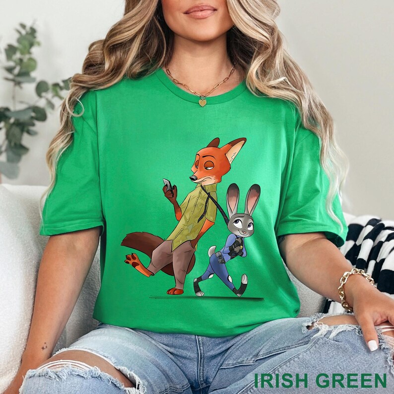 May include: Irish green t-shirt featuring a cartoon illustration of Nick Wilde and Judy Hopps from Zootopia. The fox is holding a phone, and the bunny is pulling him along. The text "IRISH GREEN" is at the bottom.
