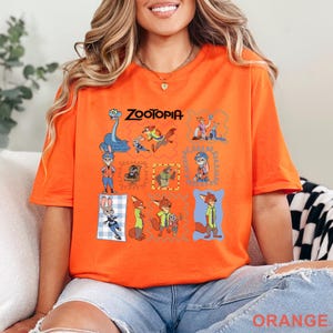 K&ouml;nnte beinhalten: Ein orangefarbenes T-Shirt mit einem Grafikdruck verschiedener Charaktere aus dem Film Zoomania, darunter Judy Hopps und Nick Wilde, angeordnet in einer Collage aus bunten Rahmen mit dem mittig platzierten Zoomania-Logo.