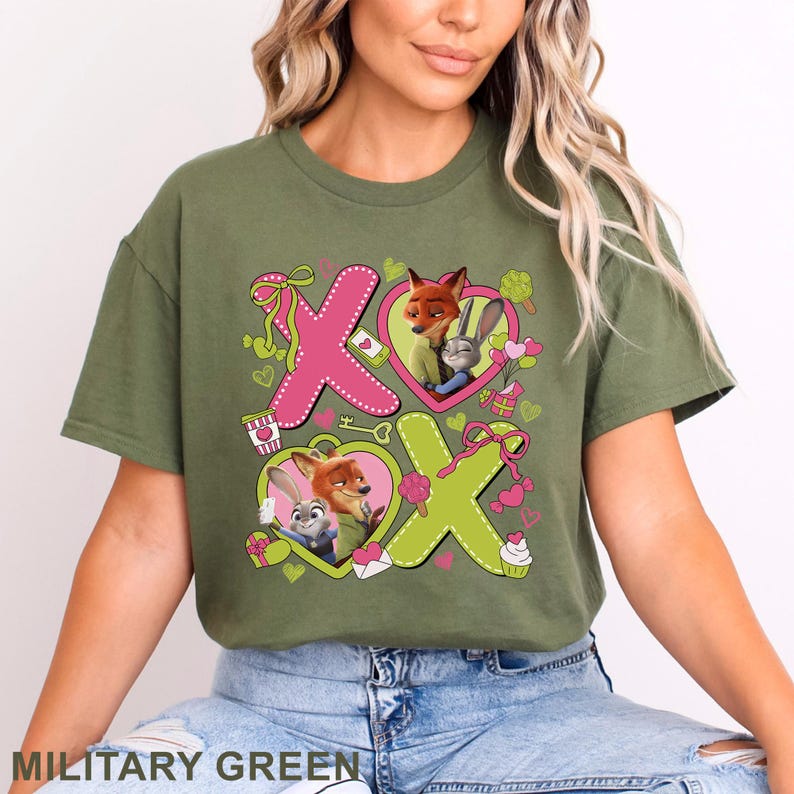 Peut inclure: Un t-shirt vert olive avec une impression graphique des personnages Nick Wilde et Judy Hopps de Zootopie. Le motif comprend de grandes lettres roses et vert citron formant XOXO, des c&oelig;urs, des petits cadeaux et diverses friandises.