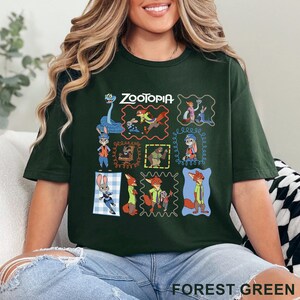 K&ouml;nnte beinhalten: Ein waldgr&uuml;nes Kurzarm-T-Shirt mit einem Grafikdruck verschiedener Charaktere aus dem Film Zoomania. Das Design enth&auml;lt mehrere gerahmte Szenen mit Judy Hopps, Nick Wilde und anderen Charakteren sowie den Schriftzug Zootopia im oberen Bereich.