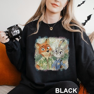 Puede incluir: Sudadera negra con un gr&aacute;fico colorido de un zorro y un conejo. El zorro lleva una camisa verde y el conejo un uniforme de polic&iacute;a azul. La palabra "BLACK" est&aacute; impresa en la parte inferior.