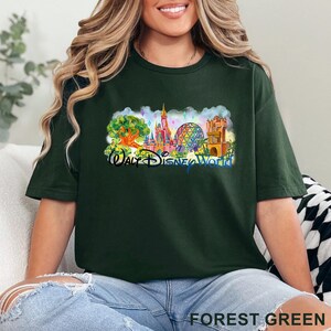 May include: A forest green short-sleeve t-shirt featuring a colorful graphic print of the Walt Disney World theme park landmarks, including the castle, the geodesic sphere, and a large tree, with the text Walt Disney World printed in blue.